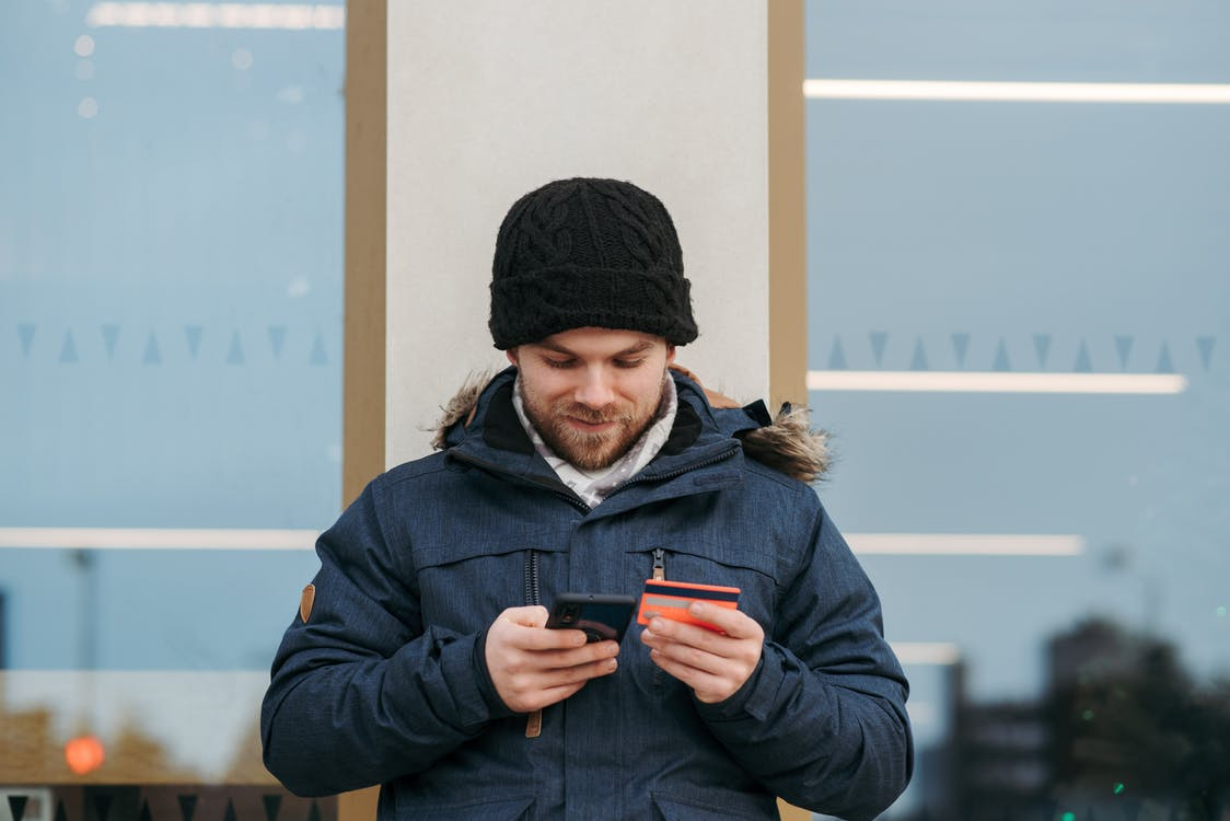 A Man Leaning Against a Wall and Entering His Credit Card Information on a Smartphone