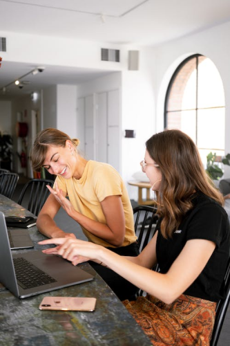 An image of two women talking while working on their laptops