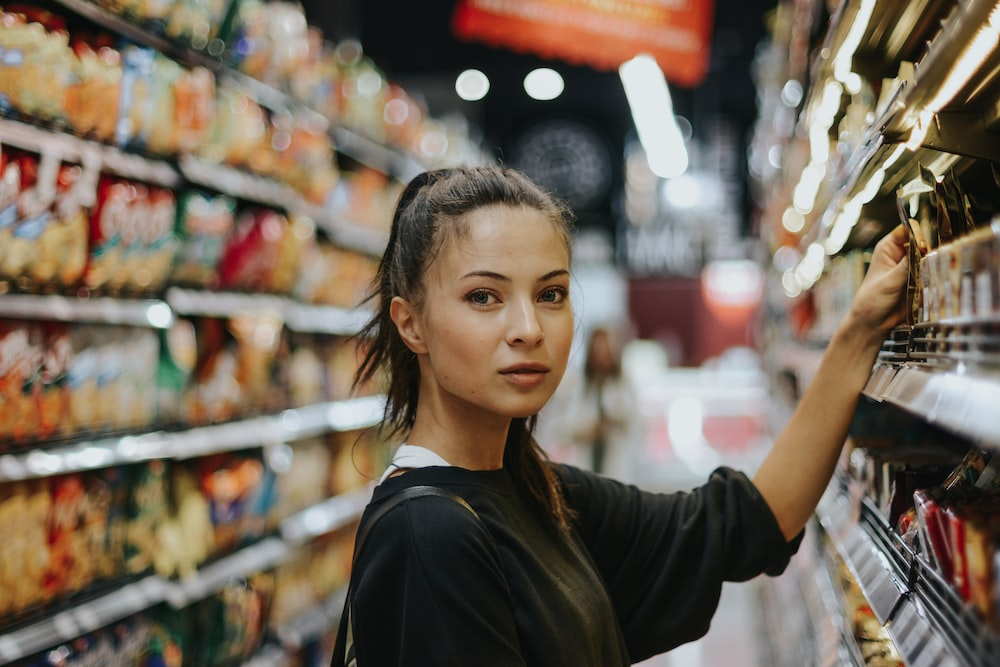 Young woman selecting items from a grocery store shelf, reflecting consumer decision-making in a retail environment.