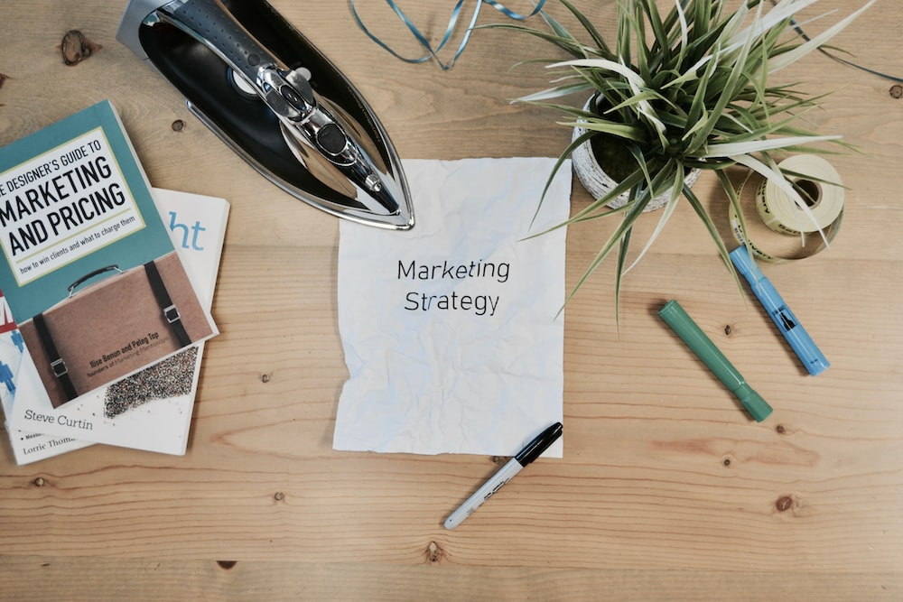 A crumpled paper with 'Marketing Strategy' written on it, surrounded by marketing books and office supplies, representing the planning phase in marketing.
