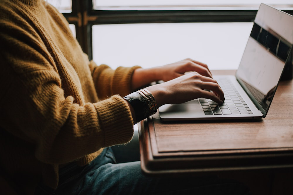 A person in a mustard sweater using a laptop, placed on a wooden table