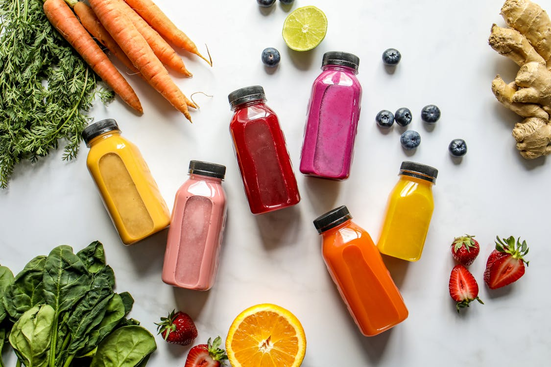 organic-beverages-ingredients Colorful bottles with smoothies beside Carrots, Ginger, Leaves and Berries