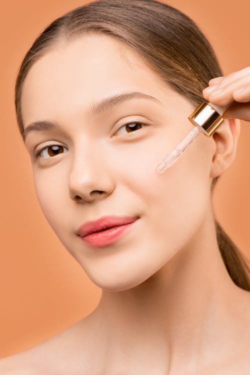 A woman with pink lipstick holding a dropper to her face with a skincare product