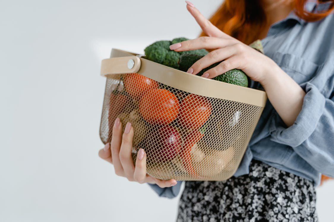 An image of a person carrying a basket with fruits and vegetables 