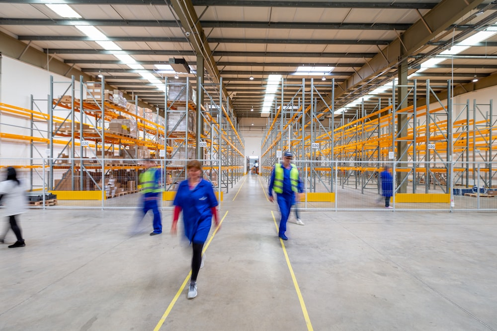 Workers in a warehouse walking along the marked aisles between storage racks.