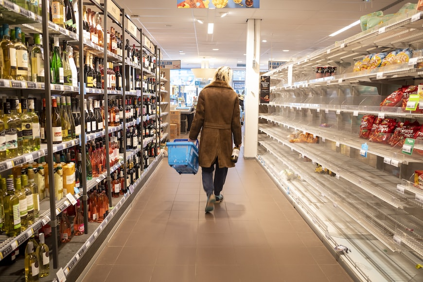 Consumer walking through a supermarket aisle with empty shelves, highlighting supply challenges.