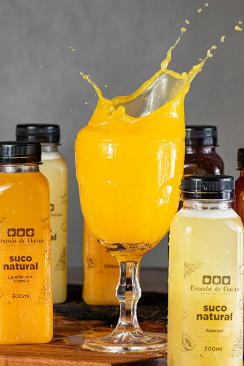 : Splash of Fresh Orange Juice in a glass with juice bottles of “Suco natural” all around