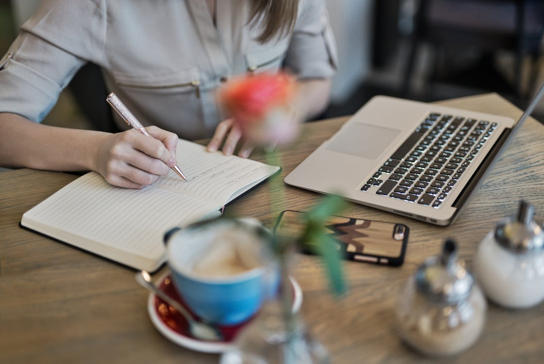 A woman writing notes on a notepad with a laptop beside her