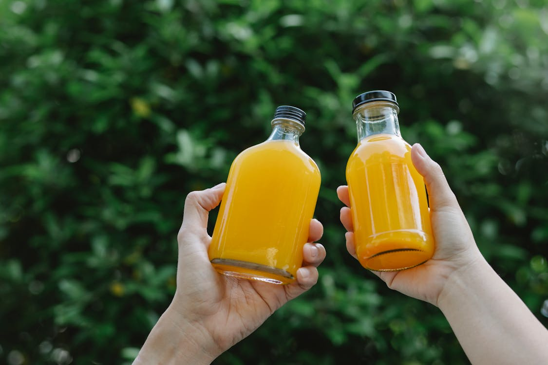 A closeup of two orange organic beverages in a person’s hands