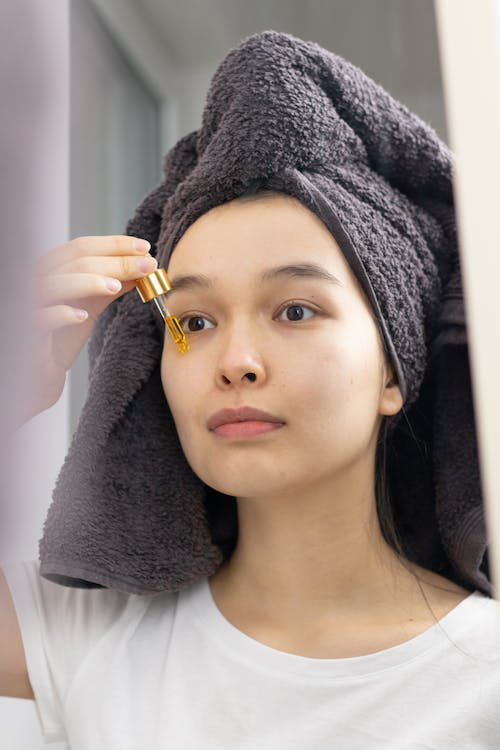 A woman with a gray bath towel on her head applying a face serum