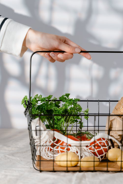 An image of a person carrying a steal basket with fruits and vegetables